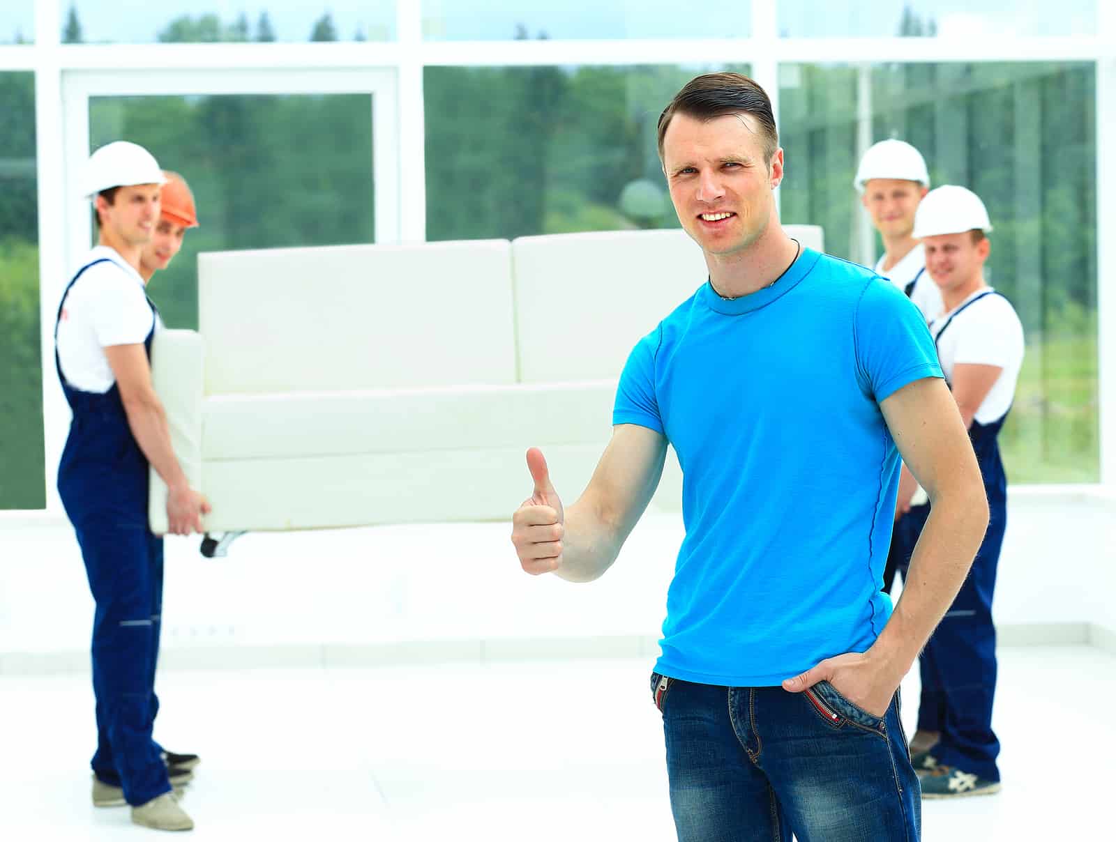 happy male movers in uniform carrying white sofa